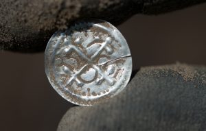 dpatopbilder - 13.04.2018, Mecklenburg-Vorpommern, Schaprode: Ein Kreuzbrakteate unter Harald Blauzahn (936-984); erster eigenständiger Münztyp Dänemarks hält eine Archäologe nach der Ausgrabung.