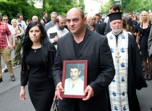 Bayern, München: Gavriil Voulgaridis (M), der Bruder des Opfers, dessen Frau Christina (l) und der orthodoxe Erzpriester Apostolos Malamoussis (r) gehen mit einem Bild des Ermordeten Boulgarides zu einer Gedenkveranstaltung mit Kranzniederlegung am Tatort. Am 15.06.2005 wurde der Grieche Theodoros Boulgarides in seinem Laden in der Trappentreustraße von Mitgliedern der Terrorzelle NSU ermordet. (Foto: dpa)