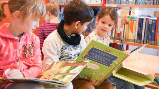Kinder schauen sich Bücher an. (Foto: dpa)