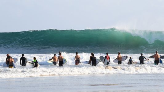 17.02.2018, Australien, Queensland, Gold Coast: Wellenreiter stehen nahe den Snapper Rocks vor der Brandung. Die großen Wellen des Pazifik an der Ostküste sind auch ein Ergebnis des Tropen-Sturms Gita, der vor wenigen Tagen auf den Inseln von Tonga Zerstörungen anrichtete. Surfer freuten sich über hohe Wellen an der Ostküste von Australien. ACHTUNG: Dieses Bild hat dpa auch im Bildfunk gesendet. Foto: Dave Hunt/AAP/dpa - Honorarfrei nur für Bezieher des Dienstes dpa-Nachrichten für Kinder +++ dpa-Nachrichten für Kinder +++