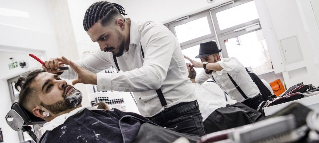 Barbier Onay Temel (M) bearbeitet mit einem Rasiermesser den Bart von Sekran (l). (Foto: dpa)