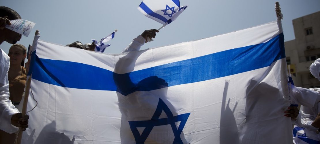 19.04.2018, Israel, Tel Aviv: Ein Feiernder schwenkt eine israelische Flagge hinter einer großen Fahne am 70. Unabhängigkeitstag des jüdischen Staates.