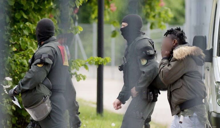 In der Landeserstaufnahmeeinrichtung für Flüchtlinge (LEA) wird ein Mann von maskierten Polizisten eskortiert. (Foto: Stefan Puchner/dpa)