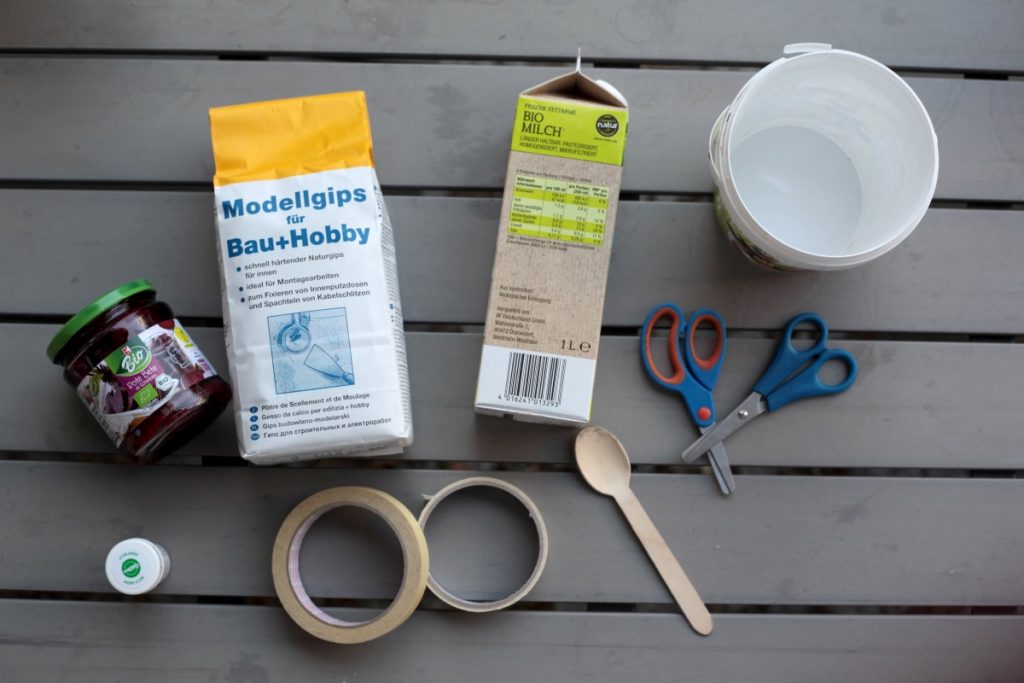 Die Materialien für Straßenkreide: Gips, Lebensmittelfarbe, ein Eimer zum Umrühren, Klebeband, Tetrapak. Straßenkreide kann man aus wenigen Materialien selbst herstellen. Foto: Corinna Schwanhold/dpa